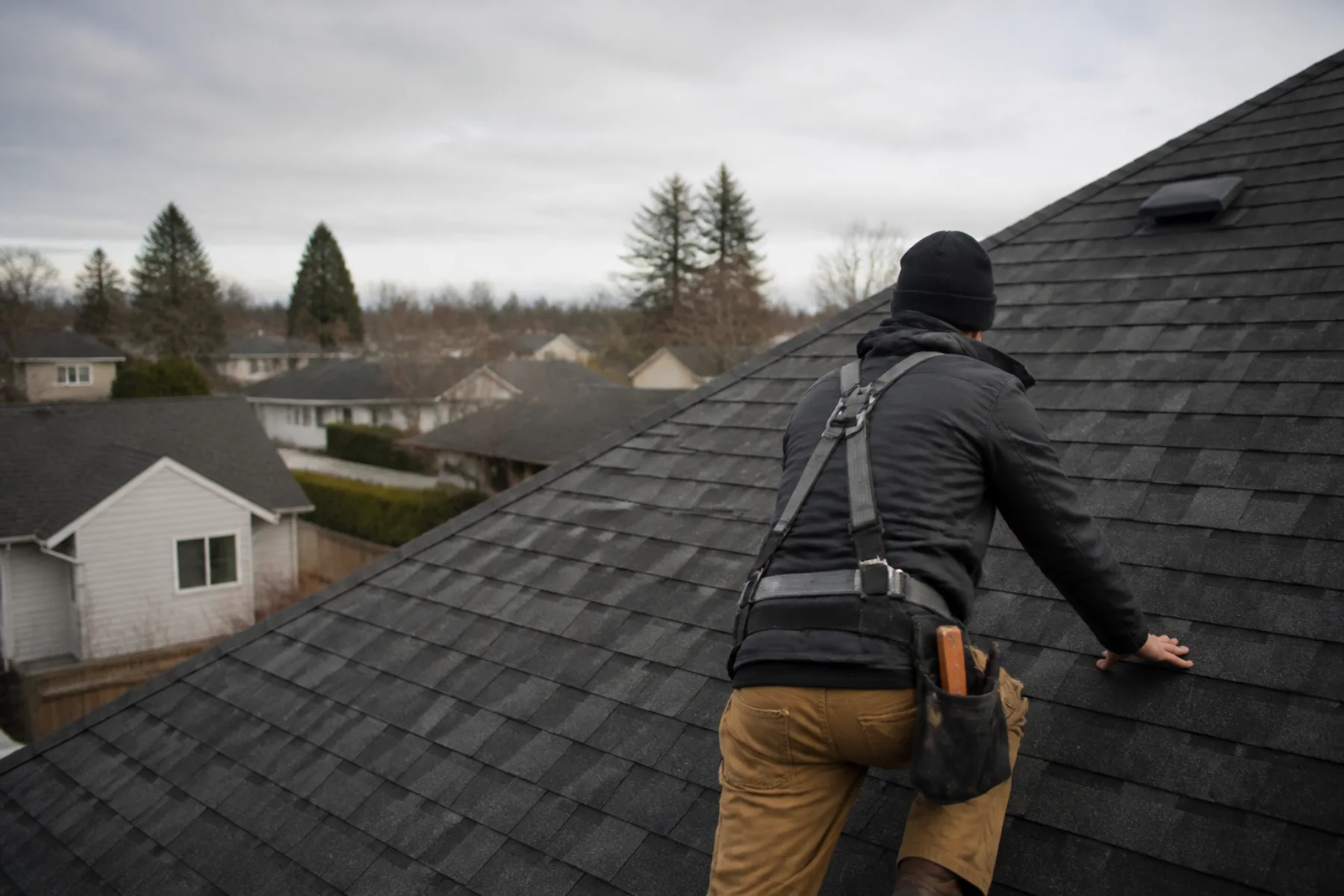 A roofer inspecting asphalt shingles on a residential roof