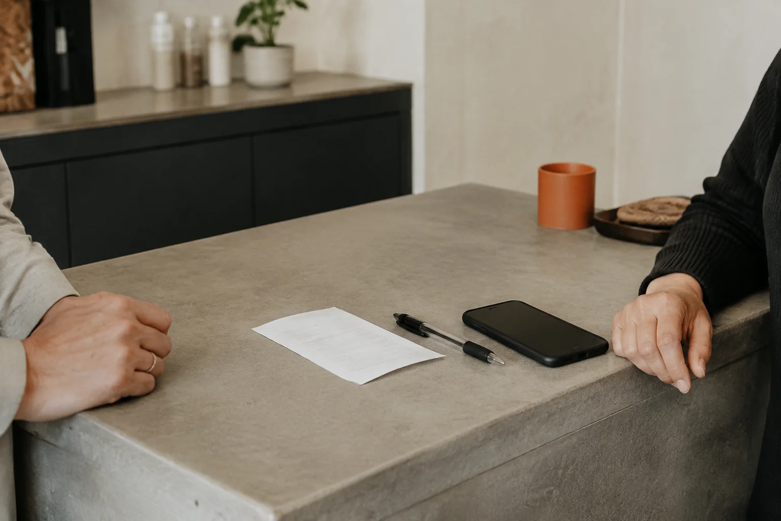 A customer and staff member at a service counter with a receipt, pen and phone